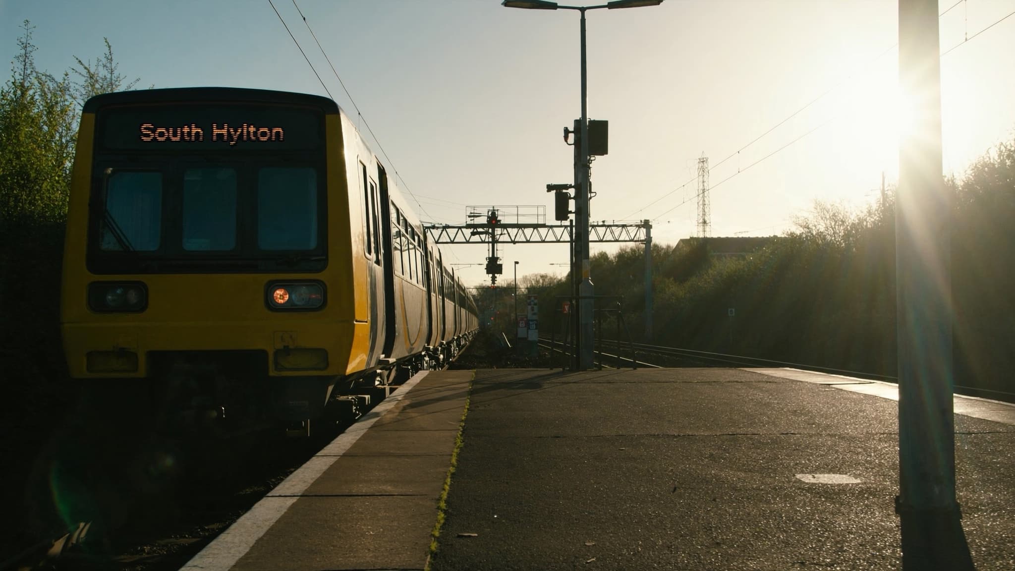 A Tyne and Wear Metro train waiting at a suburban platform in golden evening light